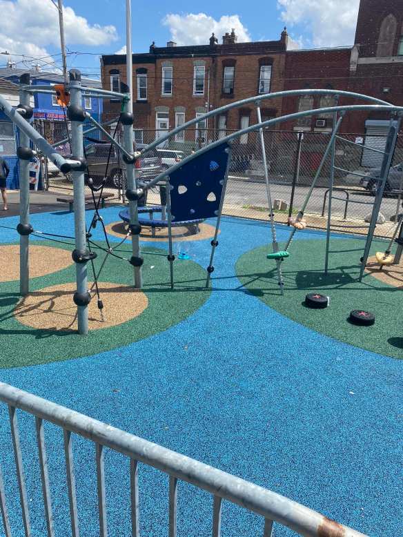 Modern playground next to pool with sprinkler on to minimize heat in direct sun